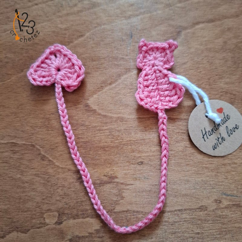 Un marque-pages plat en forme de chat rose, crocheté avec du fil coton.